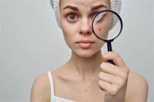 زنی با حوله ای بر سر که با زره بین جوش هایش را بررسی می کند