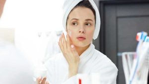 زنی حوله پوش در حال کرم زدن به پوست صورتش